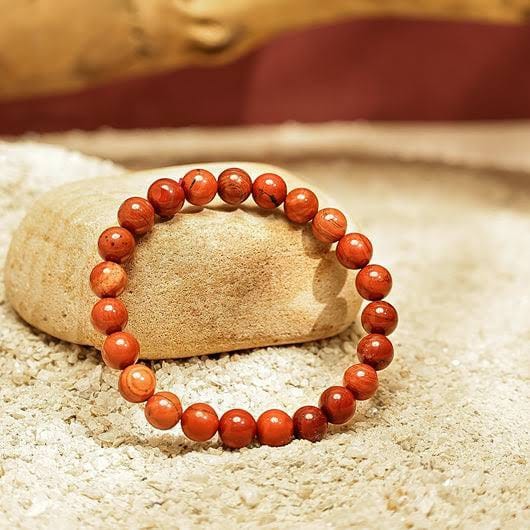 Red Jasper bracelet resting on a stone in sand